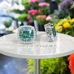 Load image into Gallery viewer, Ocean Radiance: Lustrous Cushion Cut Cyan Blue Moissanite Earrings in a Sparkling Halo.
